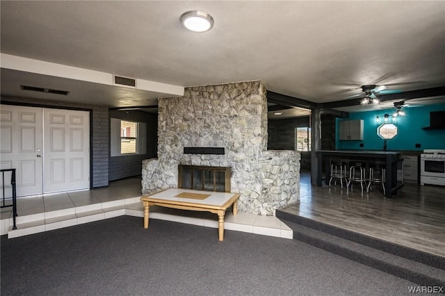 carpeted living room with a ceiling fan, tile patterned flooring, visible vents, and a stone fireplace