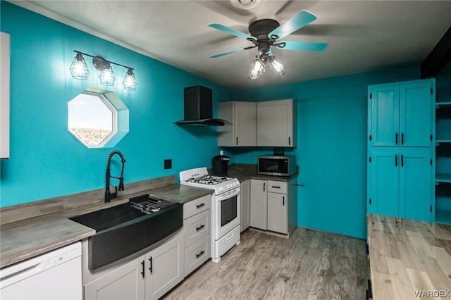 kitchen featuring light wood-style flooring, white appliances, a sink, white cabinets, and wall chimney exhaust hood