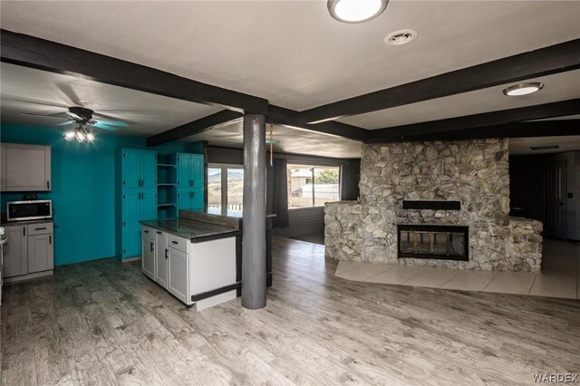 kitchen with a fireplace, light wood finished floors, dark countertops, stainless steel microwave, and white cabinets