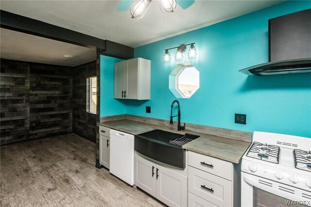 kitchen with white cabinets, a sink, wall chimney range hood, light wood-type flooring, and white appliances