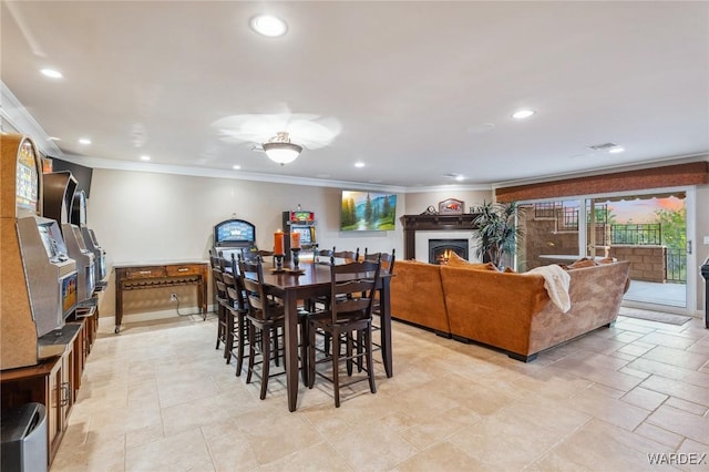 dining area with a warm lit fireplace, visible vents, ornamental molding, and recessed lighting