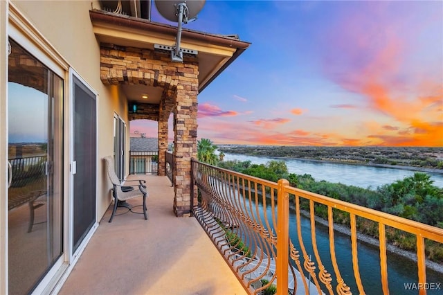 balcony at dusk featuring a water view