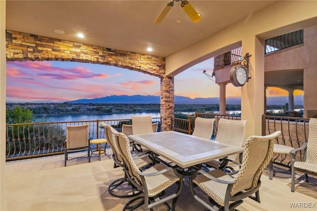 patio terrace at dusk with ceiling fan, outdoor dining area, and a water and mountain view