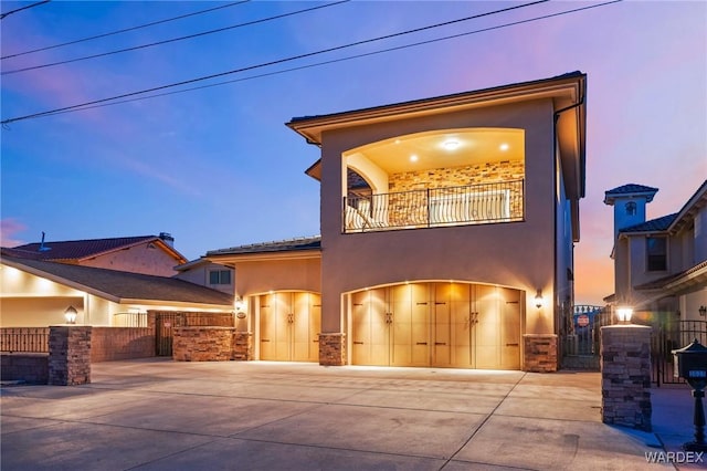 mediterranean / spanish house with stucco siding, concrete driveway, an attached garage, a gate, and a balcony