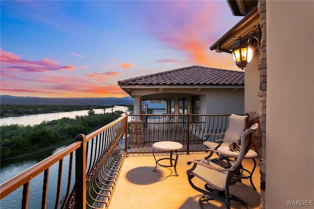 balcony at dusk featuring a water view