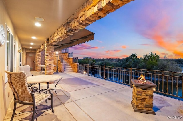 patio terrace at dusk featuring a water view, a fire pit, and stairs