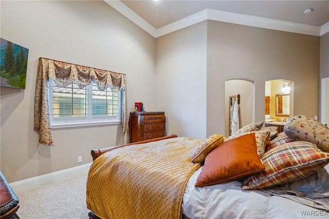 bedroom featuring arched walkways, crown molding, ensuite bathroom, carpet flooring, and baseboards