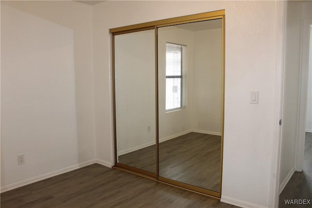 unfurnished bedroom featuring dark wood-style floors, a closet, and baseboards