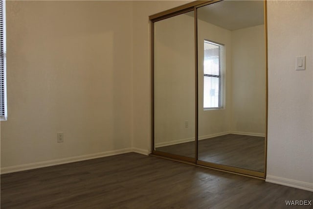 unfurnished bedroom with baseboards, dark wood finished floors, and a closet