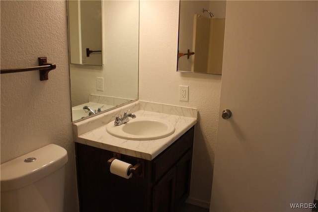 bathroom with a textured wall, vanity, and toilet