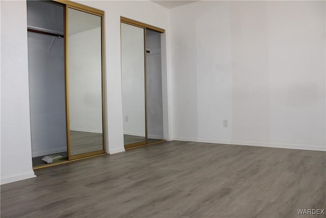 unfurnished bedroom with baseboards, wood finished floors, and multiple closets