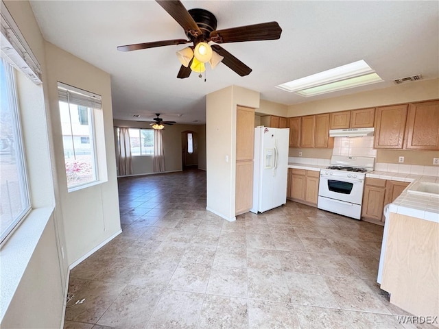 kitchen with tile countertops, visible vents, white appliances, under cabinet range hood, and baseboards