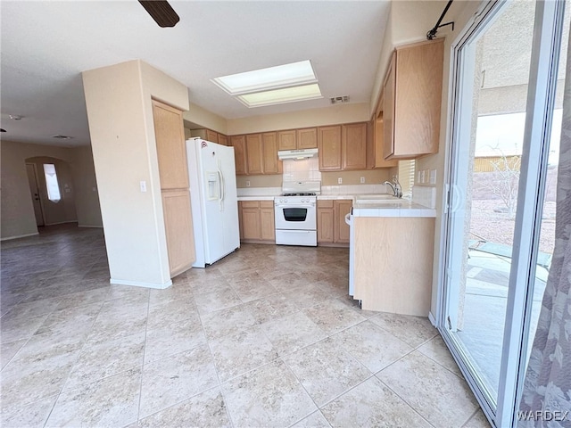 kitchen with arched walkways, under cabinet range hood, white appliances, a sink, and visible vents