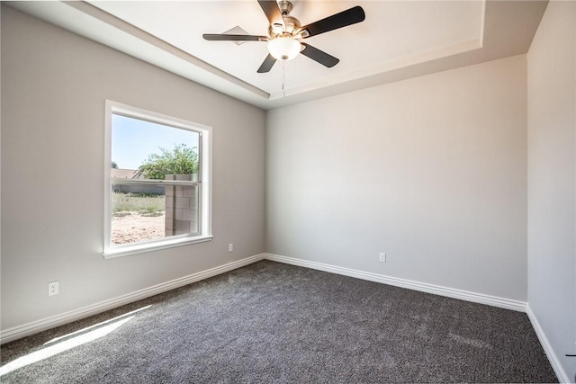 spare room featuring dark carpet, a raised ceiling, baseboards, and a ceiling fan