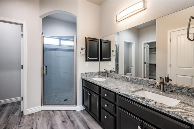 full bath featuring a shower stall, wood finished floors, baseboards, and double vanity