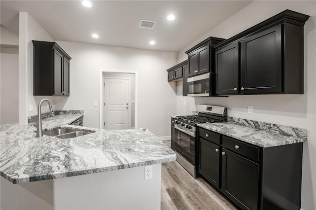 kitchen with stainless steel appliances, a sink, dark cabinetry, a peninsula, and light wood finished floors