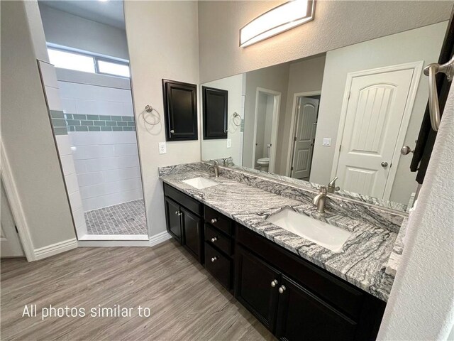 3371 N Apache St, Kingman, AZ 86401 - bathroom featuring wood finished floors, tiled shower, toilet, baseboards, and double vanity