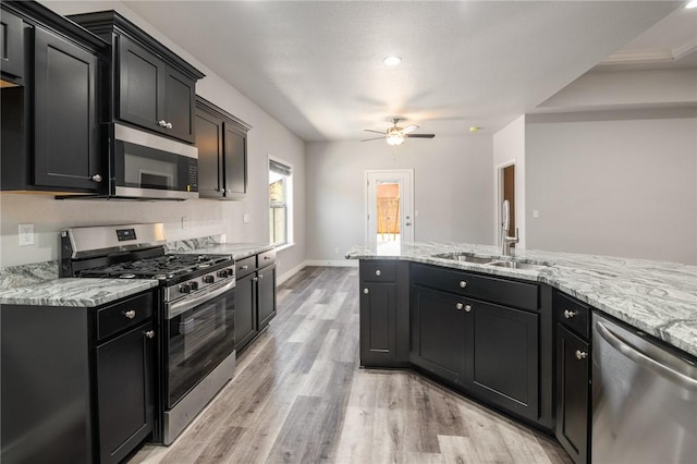 kitchen featuring stainless steel appliances, a sink, a ceiling fan, light wood-style floors, and light stone counters