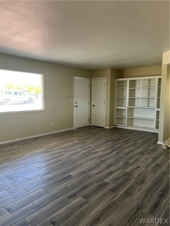 unfurnished room featuring dark wood-style flooring, a textured ceiling, and baseboards