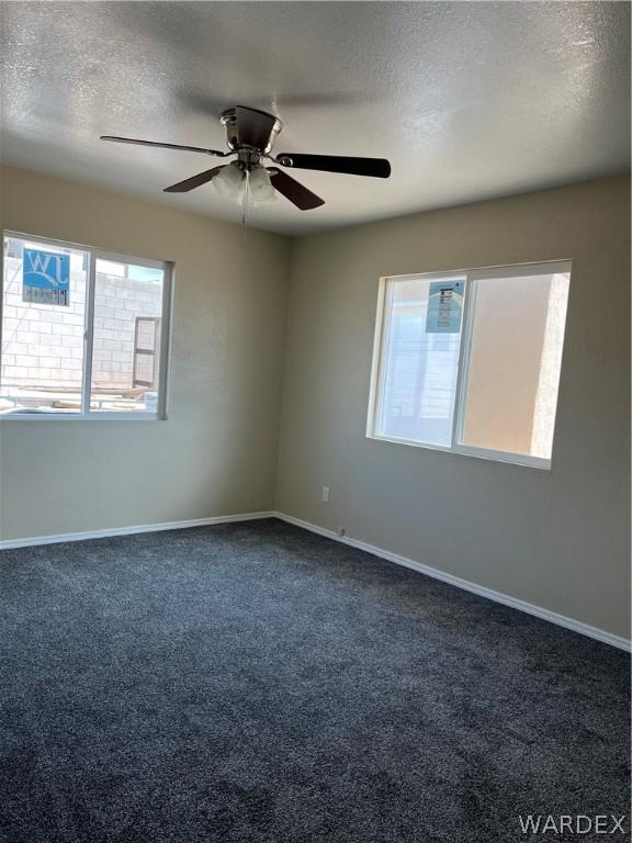 unfurnished room with a ceiling fan, dark colored carpet, a textured ceiling, and baseboards