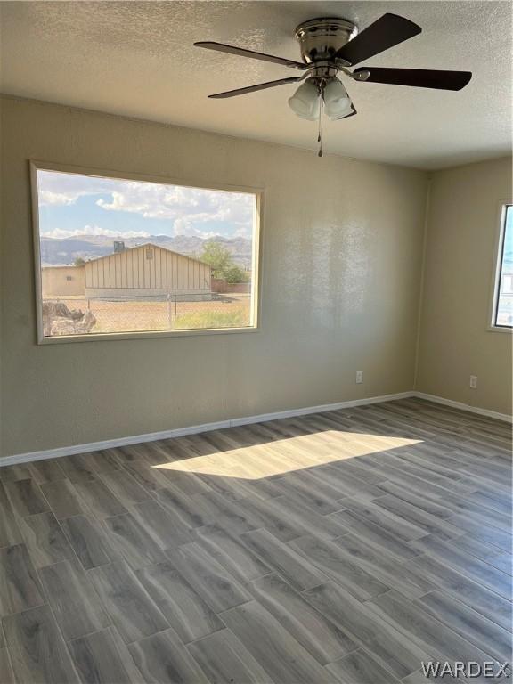 empty room with a ceiling fan, a textured ceiling, baseboards, and wood finished floors