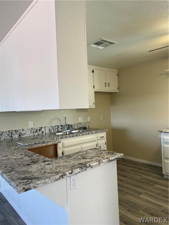 kitchen featuring light stone countertops, visible vents, white cabinets, and a sink