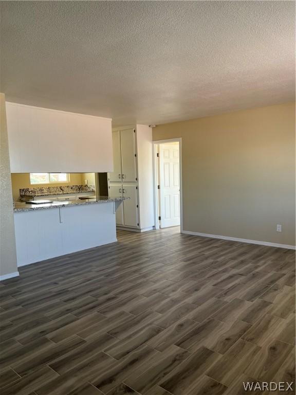 interior space featuring dark wood-style floors, white cabinets, a peninsula, and a textured ceiling