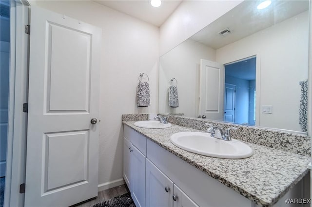 bathroom featuring double vanity, wood finished floors, a sink, and visible vents