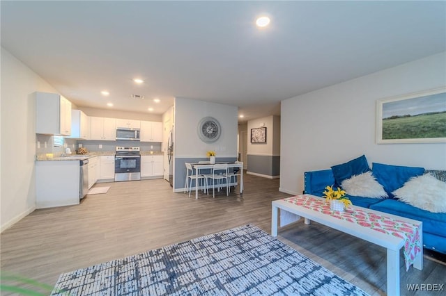 living room featuring baseboards, recessed lighting, visible vents, and light wood-style floors