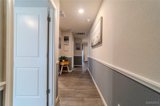 corridor featuring dark wood-style floors, baseboards, visible vents, and a textured wall