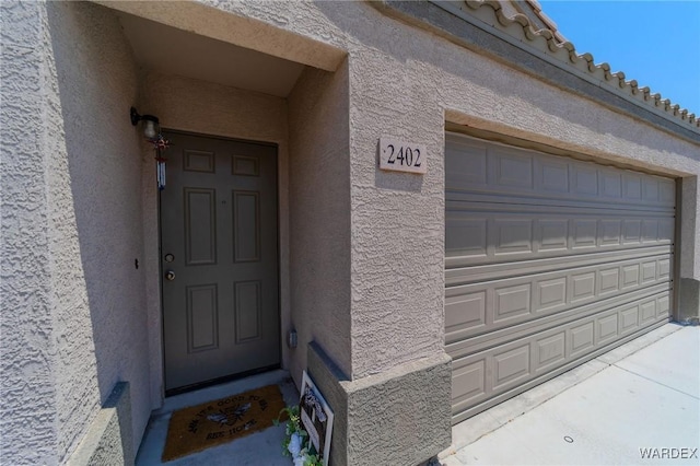 doorway to property featuring a garage, stucco siding, and a tiled roof