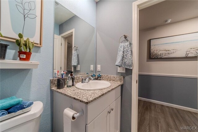 bathroom featuring toilet, baseboards, wood finished floors, and vanity