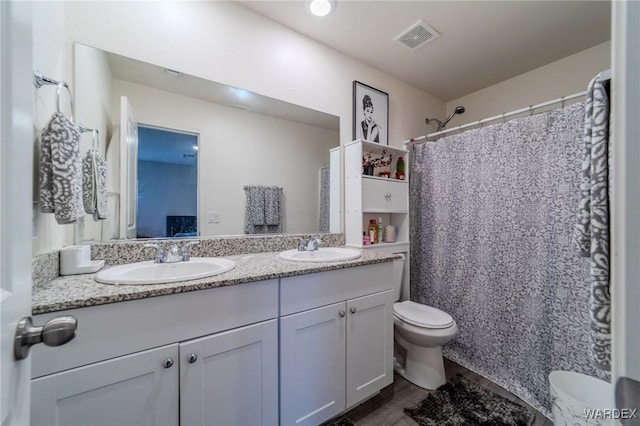 ensuite bathroom featuring toilet, double vanity, a sink, and visible vents