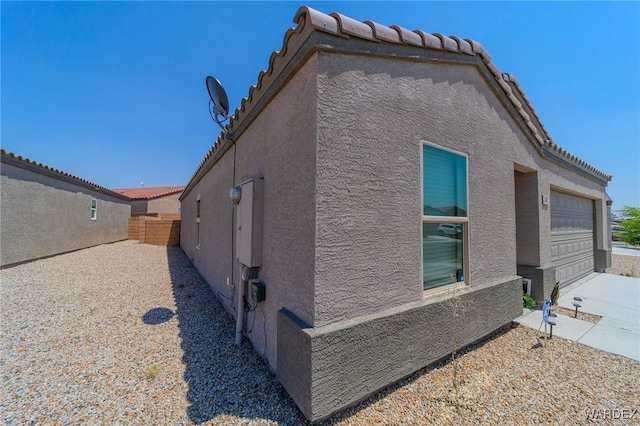 view of side of property with a tiled roof, fence, and stucco siding