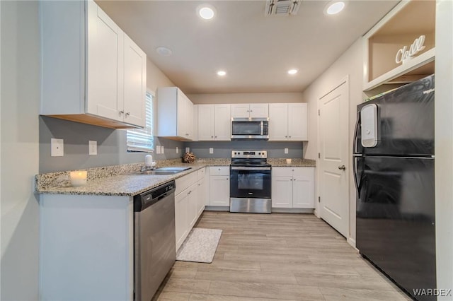 kitchen featuring light stone counters, stainless steel appliances, a sink, visible vents, and white cabinetry