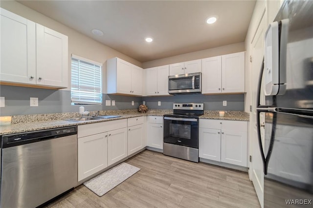 kitchen with stainless steel appliances, light stone counters, a sink, and white cabinetry