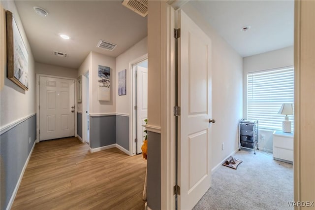 hall with light wood finished floors, visible vents, and baseboards