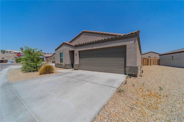 view of front of house featuring concrete driveway, a tile roof, an attached garage, fence, and stucco siding