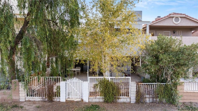 obstructed view of property with a tiled roof, a fenced front yard, a gate, and stucco siding