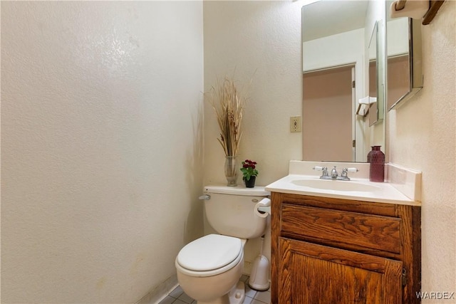 bathroom featuring toilet, a textured wall, tile patterned flooring, and vanity