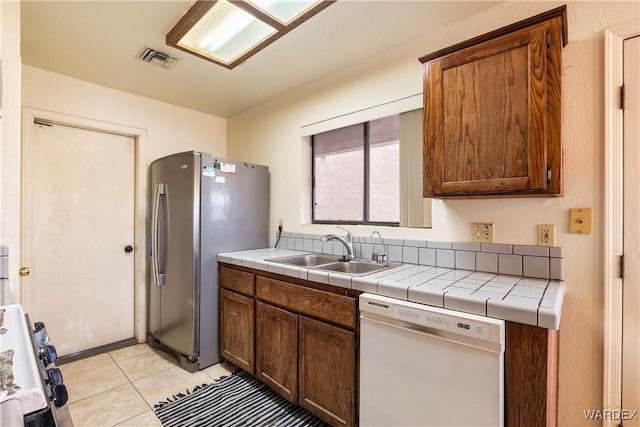 kitchen with tile countertops, freestanding refrigerator, a sink, range, and dishwasher