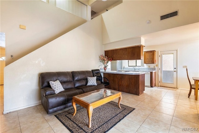 living area featuring light tile patterned floors, a towering ceiling, visible vents, and baseboards