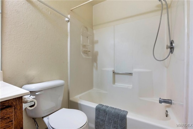 bathroom featuring a textured wall, bathtub / shower combination, vanity, and toilet