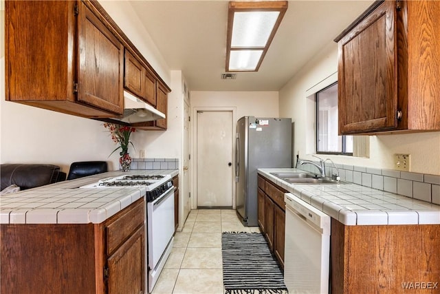 kitchen with white appliances, light tile patterned floors, visible vents, tile countertops, and a sink