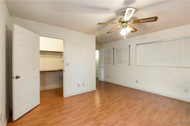 unfurnished bedroom with light wood-style floors, a walk in closet, baseboards, and a ceiling fan