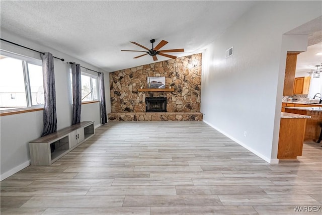 unfurnished living room with a fireplace, vaulted ceiling, a textured ceiling, a sink, and ceiling fan