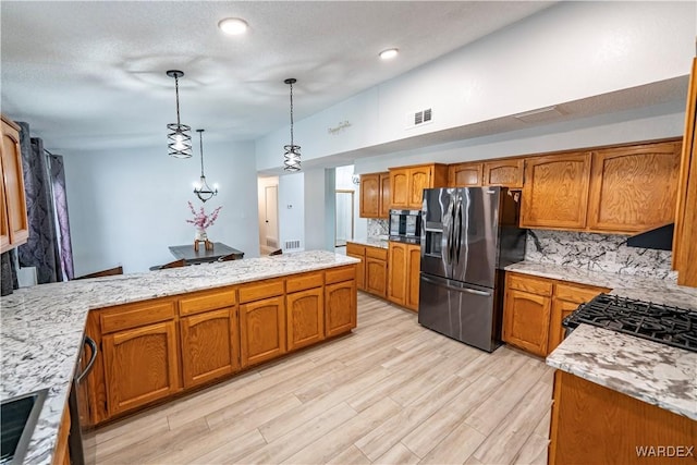 kitchen with visible vents, light wood-style floors, hanging light fixtures, appliances with stainless steel finishes, and brown cabinets