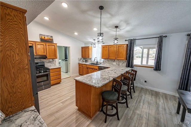 kitchen with washer / dryer, appliances with stainless steel finishes, brown cabinets, a peninsula, and a sink