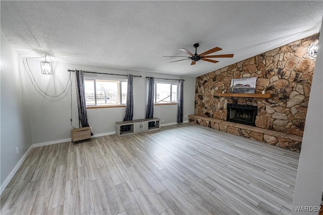 unfurnished living room with lofted ceiling, a ceiling fan, a stone fireplace, a textured ceiling, and wood finished floors