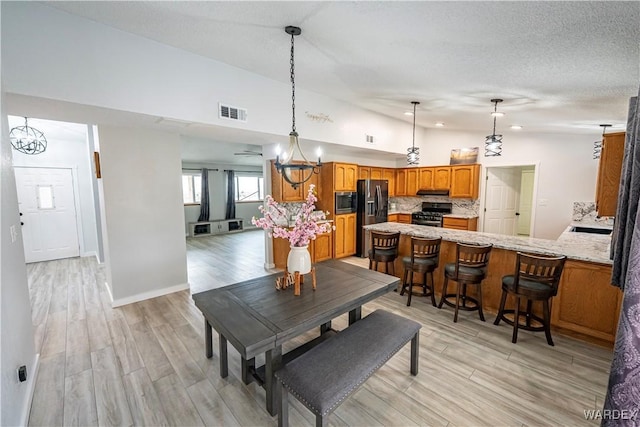 dining room with lofted ceiling, light wood-type flooring, visible vents, and a textured ceiling